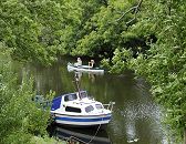 11_21604 Blick auf die Dove-Elbe bei Hamburg Reitbrook; das Ufer des Flusses ist dicht mit hohen Bumen bewachsen - die ste hngen dicht ber dem Wasser. Ein Kanu fhrt auf dem ruhigen Wasser der Doeveelbe, im Vordergrund ist ein kleines Motor-Sportboot am Bootssteg vertut. www.hamburg-fotos.org