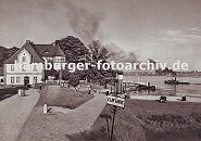 11_21622 historisches Bild vom Zollenspieker Fhrhaus ca. 1936; Spaziergnger gehen auf dem Elbdeich Richtung Gassttte; in der Bildmitte ragt das Pegelhaus am Elbstrand empor. Rechts fhrt eine Barkasse - schwarzer Qualm steigt aus ihrem Schonstein. Im Vordergrund ein schmiedeeisernes Hinweisschild "Zur Elbfhre".  www.hamburger-fotoarchiv.de