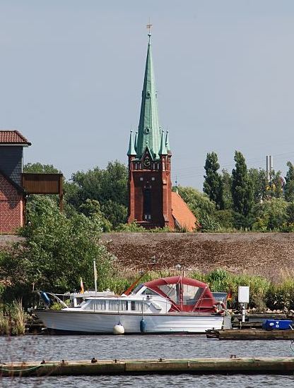 Fotografie Hamburg - Kirchturm St. Nikolai 11_21647  Der Kirchturm der St. Nikolaikirche in Hamburg Moorfleet wurde 1885 errrichte. Im Vordergrund Sportboot und Bootsstege im Holzhafen; dahinter ist der Deich zu erkennen.www.hamburg-bilder.org