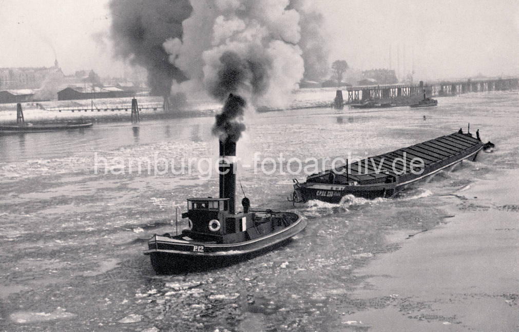 01141_33_18 Historisches Foto von der Norderelbe im Winter - Eisschollen treiben auf dem Wasser, ein Schlepper unter Dampf zieht einen Oberlnder Kahn. Im Hintergrund die Zollstation Entenwerder - niedrige Lagerhuser am Zollhafen, dahinter Wohnblocks von Hamburg Rothenburgsort.