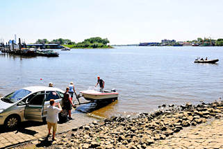 01172_2689 ffentliche Slipanlage in Entenwerder an der Norderelbe in Hamburg Rothenburgsort; ein kleines Sportboot wird von einem Bootstrailer zu Wasser gelassen. Im Hintergrund lks. die Bootstankstelle / Bunkerboot vor dem Sperrwerk Billwerder Bucht und re. das Ufer der Peute in Hamburg Veddel.