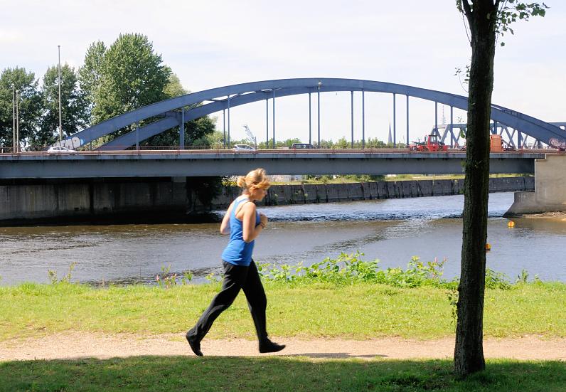 01177_5727 Joggerin auf dem Rundweg in der Grnanlage Elbpark Entenwerder - im Hintergrund die Einfahrt zum Oberhafenkanal / Billehafen sowie die Brcke der Billhorner Brckenstrasse. 