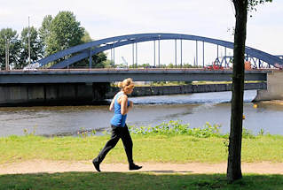 01177_5727 Joggerin auf dem Rundweg in der Grnanlage Elbpark Entenwerder - im Hintergrund die Einfahrt zum Oberhafenkanal / Billehafen sowie die Brcke der Billhorner Brckenstrasse. 