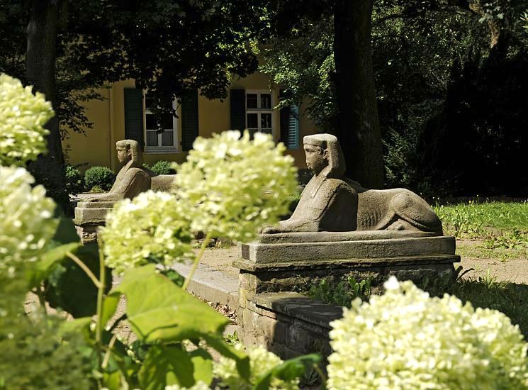 Bild vom Rathauspark in Bergedorf - Sphinxen und Hortensienblten. 11_21511 Hinter den weissen Blten von Hortensien zwei Sphinx - Skulpturen im Garten des Bergedorfer Rathauses; zwischen den Sphingen fhren in der Gartenanlage Stufen zum  Rathausgebude. Im Hintergrund ist das Bergedorfer Standesamt zu erkennen - die Fenster haben Fensterladen aus Holz.  www.hamburg-fotograf.com