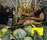 11_21541 An dem Gemsestand vom Wochenmarkt in Hamburg Bergedorf / Stadtteil Lohbrgge wird frischer Vierlnder Kohl verkauft - im Vordergrund liegen grosse Kohlkpfe Weisskohl, daneben die typischen Kohlbltter vom Wirsingkohl -  auf der linken Seite liegen der Brokkoli und der Blumenkohl. Dahinter sind Kisten mit Zwiebeln und Pappkartons mit frischen Eiern. Die Markthndlerin reicht dem Kunden seinen Einkauf, er gibt ihr das Geld fr das gekaufte Gemse. www.hamburg-fotograf.com