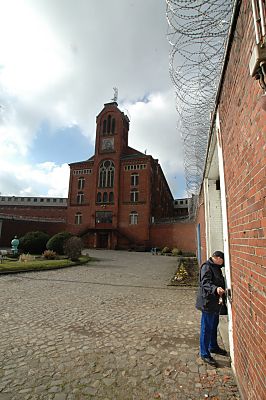 04_23330 Innenhof mit Kopfsteinpflaster; ein Vollzugsbeamter ffnet eine Tr in der Gefngnismauer. 