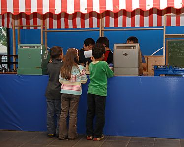 011_15914 - SKinder spielen an einem Kaufmannsladen mit rot weisser Markise, Registrierkasse und Tafel. 