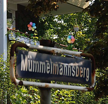 011_15992 - Namensschild mit rostiger Kante; auf dem Balkon drehen sich bunte Windrder.