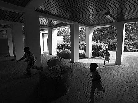 011_15603 - drei Kinder laufen in einem  Durchgang; grosse Findlinge / Felsen und Pfeiler bringen ein sdlndisches Ambiente - der Boden ist gepflastert. 