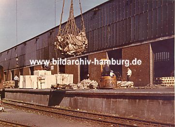 011_15280 - Stckgut auf der Laderampe vom Lagerschuppen; in einem Netz werden Scke von einem Schiff entladen. Im Vordergrund verlaufen die Schienen der Hafenbahn.