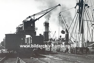 011_15282 - historisches Foto ca. 1930 - ein Schiff liegt am Kai und wird mit einem Kran entladen; Eisenbahnwaggons warten auf ihre Ladung. 