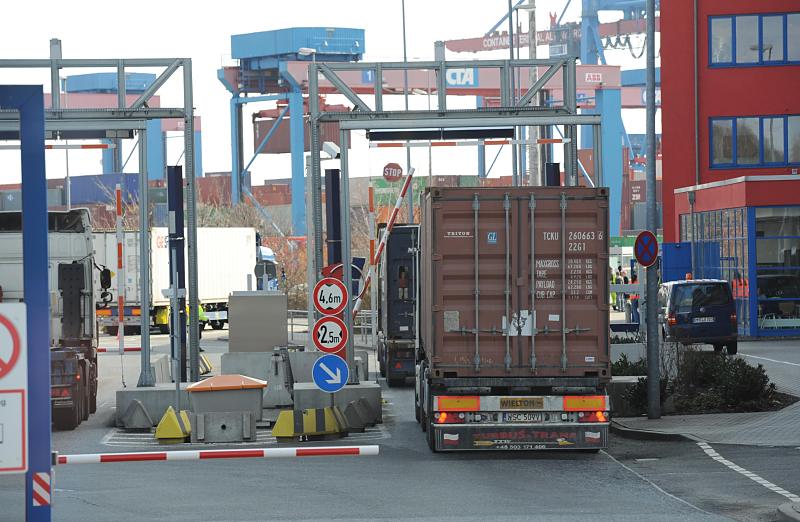 Bilder aus der Hafenstadt Hamburg - HHLA Container Terminal Altenwerder. Einfahrt Terminalgelnde Altenwerder - Sattelzge mit Ladung.  101_1117 Ein Teil der Container wird per Eisenbahn auf dem Hafenterminal Altenwerder angeliefert - eine groe Anzahl des Metallboxen kommt aber auch auf dem Trailer eines Sattelzuges zum Hamburger Hafen. Die Sattelkraft- fahrzeuge passieren die Einfahrt des Terminals - im Hintergrund sind die Portalbrcken des Container-Zwischenlagers und die Containerbrcken am Hafenkai zu sehen. 