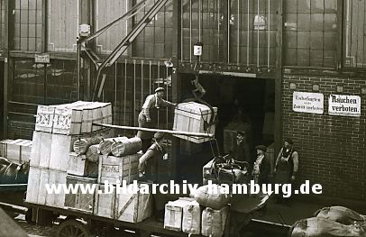 011_15821 - historische Fotografie ca. 1920; eine Ladung Kisten wurde mit Pferd und Wagen an den Hafenkai gebracht - Hafenarbeiter entladen den Wagen mit einem Kran. Schilder am Lagerschuppen: "Rauchen verboten" + "Unbefugten ist der Zutritt verboten".