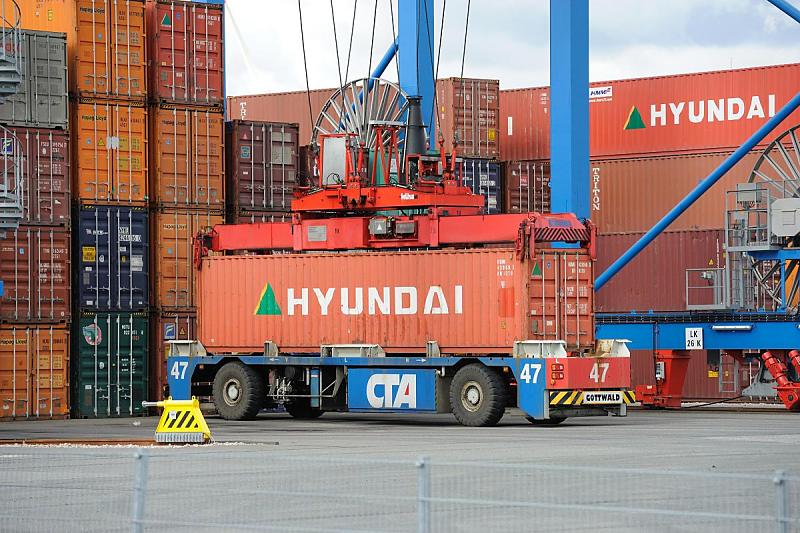 Bilder von der Arbeit im Hamburger Hafen - HHLA Container Terminal Altenwerder. Aufnahme des Containers vom AGV vor dem Containerlager. 82_0212 Vor einem den 26 Lagerblcken nimmt der Spreader des Portalkrans den Container vom Transportfahrzeug auf, um die genormte Metallbox an ihren Bestimmungsort im Containerlager zu transportieren. Jeder Containerblock des Lagers umfasst 10 Reihen  37 TEU; an jedem Platz knnen vier - in den Auenreihen fnf - Container gestapelt werden.