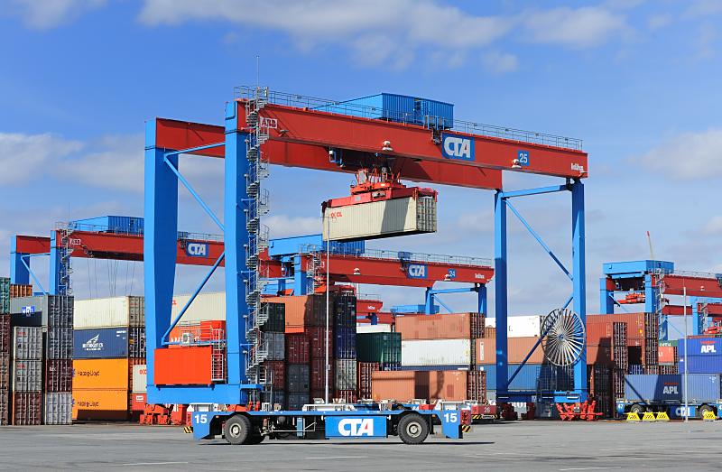 Bilder vom Containerlager - Portalkranpaar - Double Rail Mounted Gantry – DRMG Containertransport - Lagergelnde Terminal Altenwerder. 86_1146 Die Container werden mit den Automated Guided Vehicles AGV an die Krananlage des Containerlagers vom Terminal Altenwerder gebracht. Dort werden die Metallkisten vom Kran an ihen Lagerplatz gebracht. Die Krananlage abesteht aus zwei unabhngig voneinander arbeitenden Krnen (Double Rail Mounted Gantry – DRMG). Durch ihre unterschiedliche Gre knnen beide Krne simultan ber den gesamten Block arbeiten, der kleinere Kran fhrt einfach unter dem greren durch.