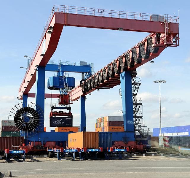 Bilder aus dem Hamburger Container-Hafen - Containerkran. Verladung von Containern auf Transport-Chassis.  90_1191 Terminaleigene Chassis und Zugmaschinen werden fr den Container-Transfer zum Bahnterminal verwendet. Einige der Fahrgestelle, die unter der Krananlage stehen, tragen schon ihre Ladung - ein weiterer Container wird gerade vom Portalkran herangebracht.