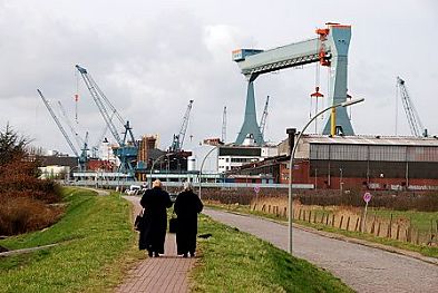 011_15405 zwei Dorfbewohnnerinnen gehen auf der Deichkone; im Hintergrund die Krne der Sietas Werft.
