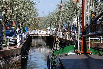 011_15466 - Fleet in Buxtehude; blhende Bume an den Kaimauern; im Hintergrund eine Brcke - re. der Bug eines Ewers, der seit ca. 1991 als Attraktion vor Anker liegt.