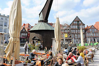 3588 Sonnentag in Stade - Café mit Tischen und Sitzplätzen auf dem Fussweg - historischer Holztretkran / Alter Kran am historischen Hansehafen.