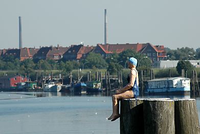 011_15740 - eine Figur mit Badeanzug und Badekappe sitzt auf einer Duckdalbe am Berliner Ufer - im Hintergrund Gebude des Hamburger Stadtteils Veddel an der Harburger Chaussee.