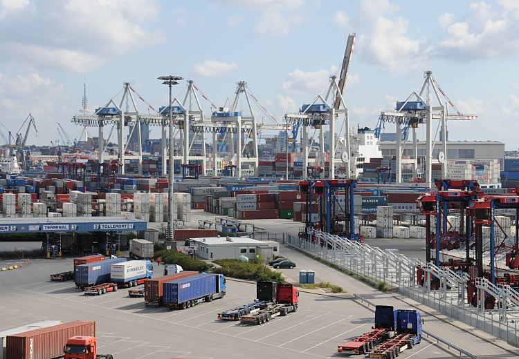 Bilder aus dem Hamburger Hafen; HHLA Container Terminal Tollerort Terminalgelände, Containerfrachter + Containerbrücken am Europakai 11_02_0507 Blick über das Gelände des HHLA Container Terminal Tollerort CTT; im Vordergrund stehen Sattelkraftfahrzeug und warten auf ihre Abfertigung. Auf dem Terminal-Areal sind die Container gelagert, die an ihren Bestimmungsort gebracht werden sollen. Am Europakai liegt ein Containerfrachter - die Containerbrücken sind herunter gefahren, nur der Ausleger über den Schiffsaufbauten ist weiterhin hochgeklappt.