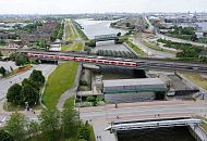 214_0043 Im Vordergrund hinter der Wilhelmsburger Brcke das Mggenburger Sperrwerk und die S-Bahnstation Veddel - ein roter S-Bahnzug steht an der Haltestelle. Die Backstein- Wohnhuser auf der linken Bildseite gehren noch zum Stadtteil Veddel, dahinter beginnt Hamburg-Wilhelmsburg. Der Spreehafen im Bildzentrum und der Hansahafen lks. sind Teil des Stadtteils Kleiner Grasbrook.