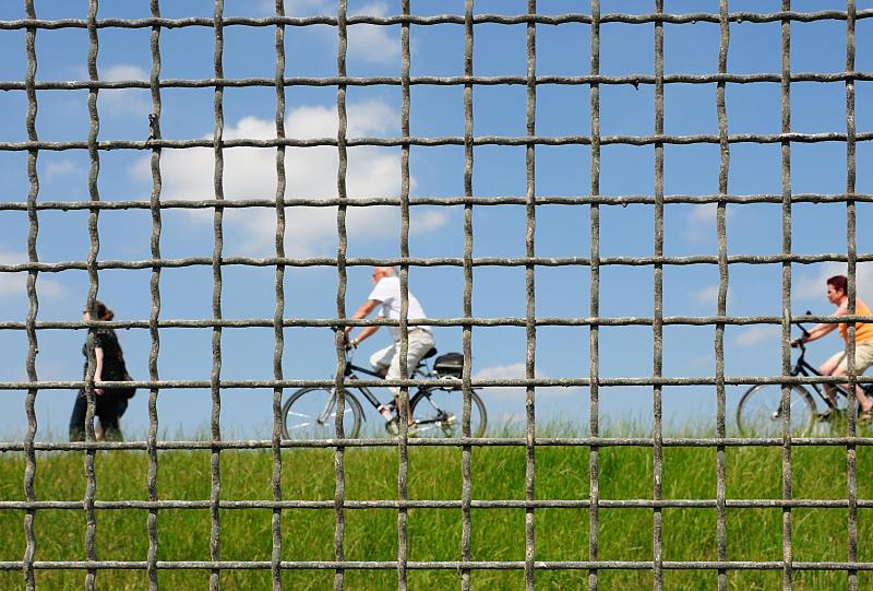 Bilder vom Hamburger Hafen / Spreehafen. Fahrradfahrer und Spaziergängerin hinter dem Zollzaun auf dem Spreehafen Deich. Hamburgfotograf Christoph Bellin. 62_9269 Der Zollzaun der das 13 Hektar große Gebiet am Spreehafen von der Nutzung durch die Anwohner abgetrennt hat zwei Durchlässe bekommen, so dass das neue Freizeitgebiet zum Fahrradfahren, spazierengehen oder rollerscaten genutzt werden kann.