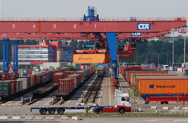 11_21383 auf sechs neben einander liegenden Bahngleisen knnen die Gterwaggons mit vier Portalkrnen beladen und entladen werden. Sattelschlepper / Tieflader bringen die Container an die Ladestation, damit sie fr den Gterverkehr verladen werden knnen. Die Portalkrane sind mit Drehkatzen ausgerstet, so dass der Gterzug schnell beladen werden kann. Rechts stehen Container auf Tiefladern und warten auf ihre Verladung - im Vordergrund fhrt ein Sattelschlepper mit leerem Chassis. Links im Hintergrund das Verwaltungsgebude der HHLA auf dem Container Terminal Altenwerder.  www.bildarchiv-hamburg.de