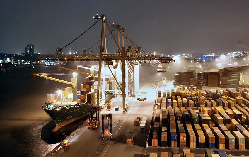 11_21439 Fotografie vom Hamburger Hafen bei Nacht - Frachter am Kai im Containerhafen Hamburg - Hafenbilder in der Nacht Blick von der Containerbrcke am Athabaskakai; ein Containerschiff liegt an der Kaimauer und wird beladen. Starke Strahler beleuchten den Frachter und das Terminal Burchardkai - ein Container wird gerade von der Containerbrcke aufgenommen, um an Bord des Schiffes gebracht zu werden; Van-Carrier bringen neue Fracht vom Containerlager. Am anderen Elbufer die Lichter der Brogebude von Hamburg Neumhlen und auf der rechten Seite die blau angestrahlten Fautrme des Klrwerks Dradenau.  www.bildarchiv-hamburg.de