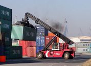 11_21440 Ein Containerstapler transportiert den 20 Fuss - Container am Spreader zu seinem Lagerplatz. Mit dem Teleskoparm knnen diese Art der Flurfahrzeuge die Metallbehlter in einer Stapelhhe von fast 16m absetzen. Eine hervorragende Wendigkeit dieser Transportfahrzeuge ist wegen der dicht gelagerten Container erforderlich - bei dem Container Radfahrzeug liegt die Lenkung auf den hinteren Rdern.   www.bildarchiv-hamburg.de