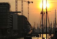 11_26039 Hoch stehen die Baukrne an der Bausstelle der Elbphilharmonie beim ehemaligen Kaispeicher A. Zwischen den Masten der Schiffe im Hamburger Traditionsschiffhafen scheint die Abendsonne. Barkassen fahren durch den Sand- torhafen Richtung Elbe.  