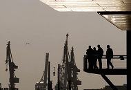 12_26042 Auf einer Aussichtsplatzform in der Hafencity stehen Hamburgtouristen und blicken ber den Sandtorhafen auf den gegenber liegenden Kaiserkai. Im Hintergrund am anderen Ufer der Elbe die Hafenkrne als Silhouette im Gegenlicht der Abenddmmerung.