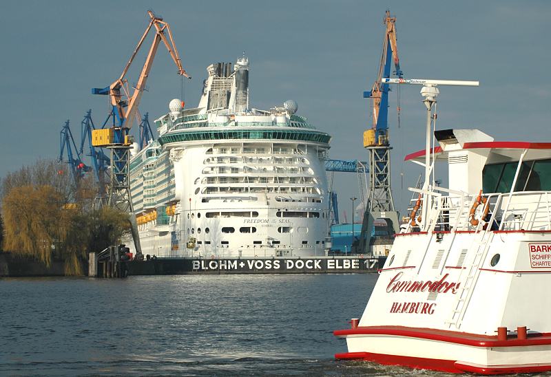 Fotografien vom Hamburger Hafen - eingedocktes Passagierschiff Dock Elbe 17. Fotoposter von Hamburg als GEschenk zum Jahrestag - Jubilum - Firmenabschied.  19_6837 Das zweitgrte Passagierschiff der Welt liegt im Trockendock der Werft Blohm + Voss. Das 2006 in Dienst gestellte Kreuzfahrtschiff hat 1800 Passagierkabinen fr 3600 Passagiere und eine Mannschaft von 1360. Im Vordergrund das Heck eines Fahrgastschiff, das gerade an den St. Pauli Landungsbrcken anlegt. www.fotograf-hamburg.de