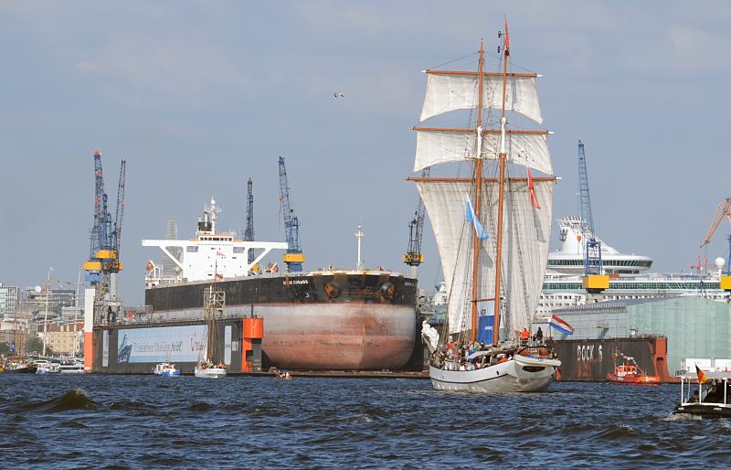 Bilder vom Hamburger Hafen + der Elbe - eingedockter Tanker OCEAN COSMOS. Fotoposter von Hamburg als GEschenk zum Jahrestag - Jubilum - Firmenabschied. 20_8173 Der 190m lange und 32m breite Tanker OCEAN COSMOS liegt im Schwimmdock 11 der Werft Blohm + Voss; Arbeitskrne stehen auf dem Werftgelnde der 1877 gegrndeten Hamburger Grosswerft. Ein Segelschiff fhrt unter Segel Richtung Landungsbrcken. www.fotograf-hamburg.de