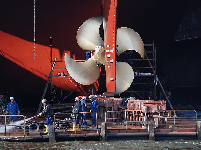 Hamburg-Bilder  aus dem Hafen - Frachter im Trockendock; Werftarbeiter + Schiffsschraube. Fotoleinwand von Hamburgbildern als Geschenk zum Jahrestag - Jubilum - Firmenabschied. 29_x9839 Die Bronzelegierung der neuen Schiffsschraube glnzt in der Sonne. Werftarbeiter reinigen das Trockendock mit einem Wasserstrahl. www.hamburg-bilder.org