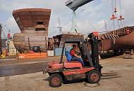 37_5045 Ein Gabelstaplerfahrer fährt sein Fahrzeug über das Werftgelände der Sietaswerft. Im Hintergrund Stahlsegmente eines Schiffsneubaus. 