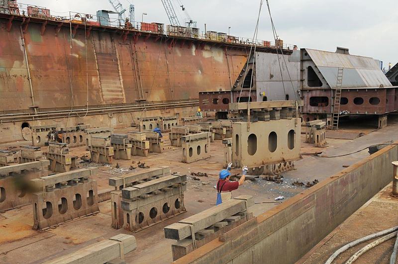 38_5166 Ein Werftarbeiter steht im Trockendock der Sietas Werft und dirigiert einen Dockblock, das mit einem Kran an in das Dock gebracht wird, an seinen Platz. Im Hintergrund zwei Schiffssektionen, die auf Dockblocks stehen.