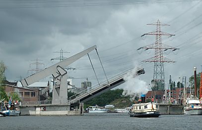 11_15777 - die Lotsekanal Klappbrcke ffnet sich um eine Barkasse durch zu lassen - aus dem Schornstein kommt Dampf; im Hintergrund die hohen Masten der Strom berlandleitungen. 