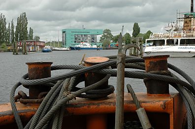 11_15793 - Schiffsheck im Harburger Werfthafen - Stahltrossen sind um die Schiffspoller geschlungen - ein Schiffshaken / Boothaken ist am Heck abgelegt; im Hintergrund das Polizeigebude der Wasserschutzpolizei im berwinterungshafen - Polizeischiffe liegen vor Anker.