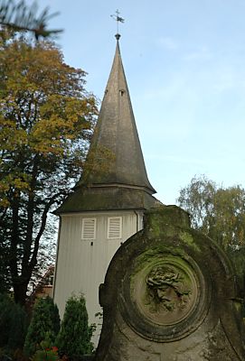 011_15054 - Grabstein mit einem Jesus - Relief / Dornenkrone; der Kirchturm mit Wetterfahne im Hintergrund.