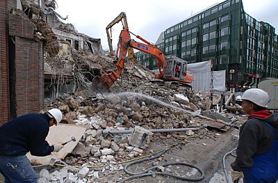 011_15150 - ein Raupenbagger zerkleinert den Bauschutt; ein Bauarbeiter spritzt Wasser mit einem Schlauch auf die Baustelle, damit die Staubentwicklung reduziert wird. 