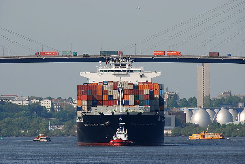 Bilder von Hamburgs Straen und Brcken Lastwagen auf der Khlbrandbrcke / Containerfrachter mit Schlepper. 05_15577 Lastwagenverkehr auf der Khlbrandbrcke; ein hoch beladener Containerfrachter fhrt mit Hilfe eines Schleppers auf dem Khlbrand und hat gerade die 53m hohe Hafenbrcke unterquert. Rechts die Faultrme der Klranlage Khlbrand und auf der anderen Seite der Elbe die Wohnhuser an der Palmaille und Elbchaussee von Hamburg Altona.