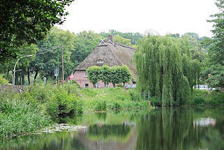 4573 Marmstorfer Feuerlschteich - Reetdach eines Bauernhauses im Hintergrund - Weiden mit ins Wasser hngenden Zweigen am Ufer des Dorfteiches.