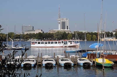 4218 Bootsverleih an der Alster - Tretboote liegen am Bootssteg - ein weisses Schiff der Alsterflotte fhrt Richtung Uhlenhorst. Im Hintergrund das Alsterufer von Hamburg Harvestehude, sowie der Fernsehturm und das Radisson Hotel Hamburg