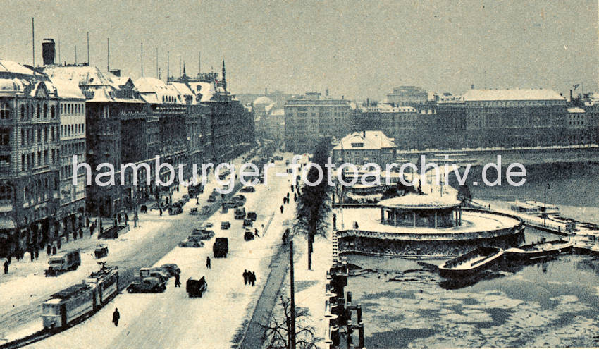 1082_76_31 Schnee liegt auf der Strasse und den Dchern der Huser; eine Strassenbahn fhrt Richtung  Gnsemarkt.  Autos parken am Strassenrand - Fussgnger gehen auf beiden Seiten der Strasse. Die Binnenalster ist mit Eisschollen bedeckt, zwei Schuten liegen vor dem Verkehrspavillon - im Hintergrund der Alsterpavillon und er Neue Jungfernstieg. 