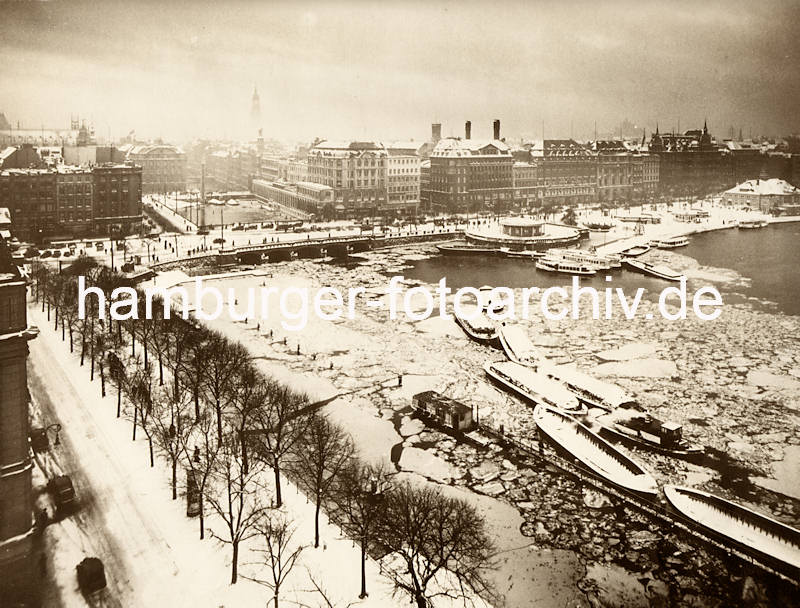 1083_X-0911-32 Blick über den Alsterdamm / Ballindamm auf das winterliche Hamburg - im Vordergrund liegen Schuten und ein Schlepper unter Dampf. Beim Verkehrspavillon haben weitere Schuten und Alsterdampfer festgemacht. . 