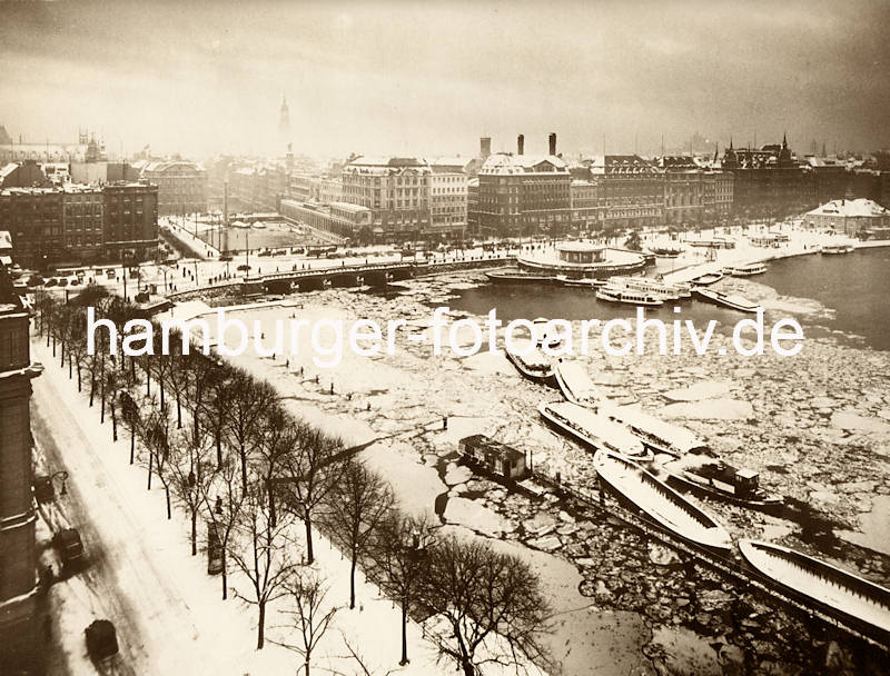 1083_X-0911-32 Blick ber den Alsterdamm / Ballindamm auf das winterliche Hamburg - im Vordergrund liegen Schuten und ein Schlepper unter Dampf. Beim Verkehrspavillon haben weitere Schuten und Alsterdampfer festgemacht. . 