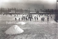 087_1_900 Der Schnee auf dem Eis auf der zugefrorenen Aussenalster ist zu grossen Haufen zusammen geschoben - Kinder laufen Schlittschuh oder glitschen ber das Eis. Ein Kind sitzt auf einem Fahrrad, das mit Kufen gesttzt wird.