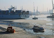 11_22730 Winter in Hamburg; Eisgang auf der Elbe und im Hamburger Hafen. Ein Containerschiff wird von einem Schlepper rückwärts in das Hafenbecken vom Tollerort Terminal gezogen. Hoch ragen die Arme der Hafenkräne in den diesigen Winterhimmel. Eine Hafenfähre bahnt sich ihren Weg durch das Eis auf der Elbe und steuert den Anleger "Dockland" an. ©www.fotograf-hamburg.de