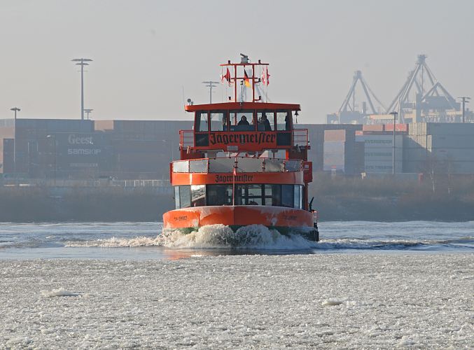 11_22731 Die Hafenfhre Tollerort  der Hamburger Fhrschiffreederei HADAG kommt von Hamburg Finkenwerder und legt am Anleger "Dockland" in Hamburg Neumhlen an. Dicht treibt das Eis auf der Elbe, noch knnen sich dieSchiffe ihren Weg durch die Eisschollen bahnen. Im Hintergrund sind auf der anderen Elbseite die Container auf dem Gelnde des Terminals Tollerort gestapelt. www.fotograf-hamburg.de Hamburg Fotografie  - Eisschollen auf der Elbe, Hafenfhre 